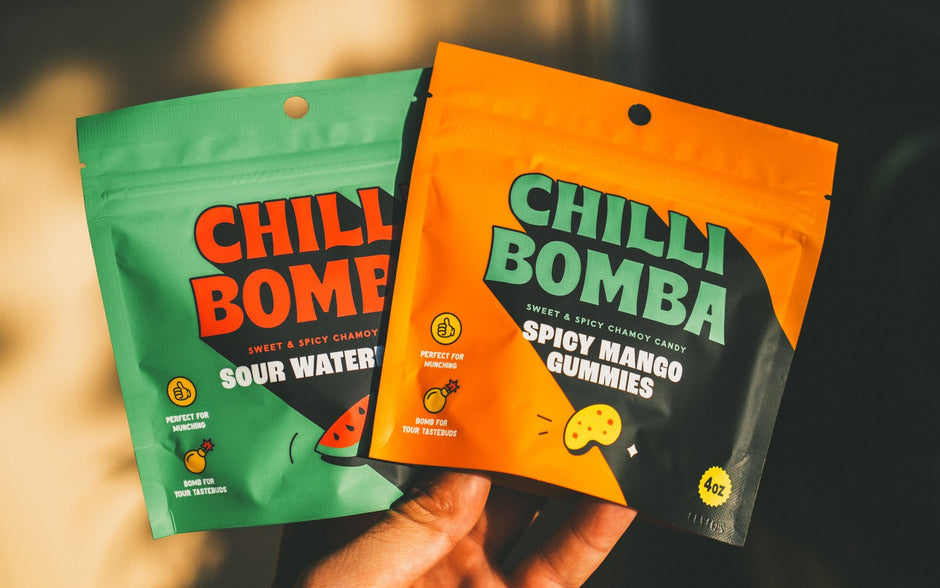 Hand holding bags of Chilli Bomba Sour Watermelon and Spicy Mango Gummies in golden light